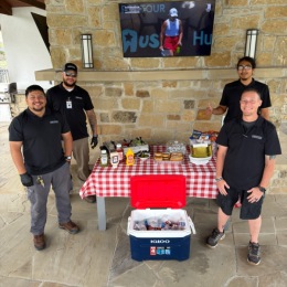 people standing next to a tv a table with food on it and a cooler full of drinks